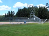 Baseball field at Klahanie Park in Sammamish surrounded by large grassy area. Coniferous trees and a power transmission utility pole are in the background.