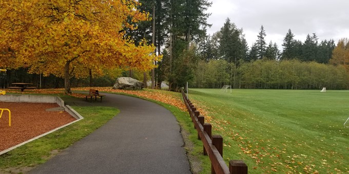 paved walkway between football field and playground, approaching a forested area