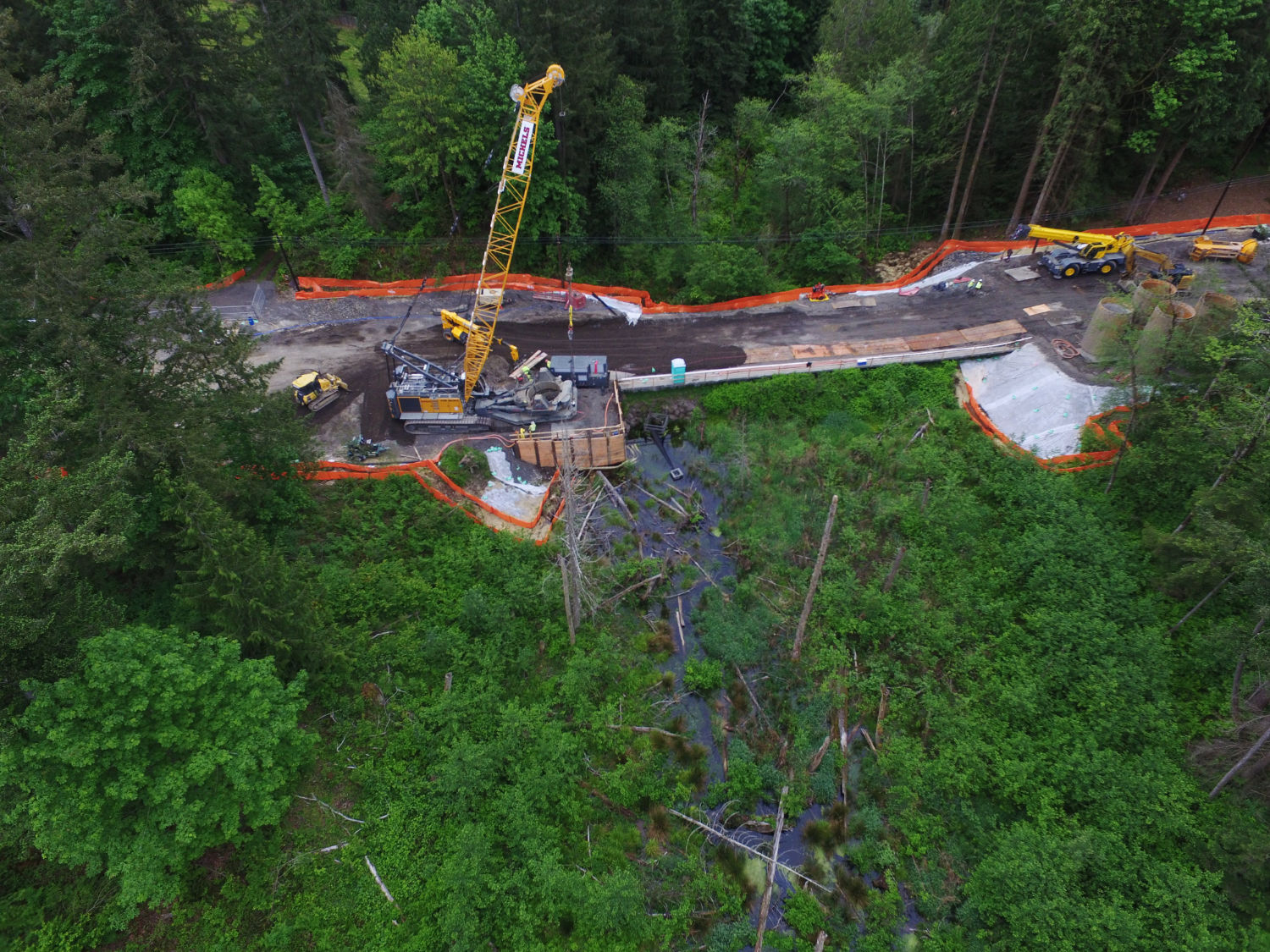 aerial view of construction on Issaquah Fall City Road over a stream or wet area with fallen logs and lush vegetation
