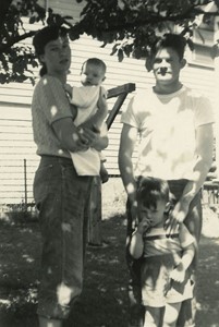 black and white photo of the Beaton Family, with a man, woman, and two children standing beneath a tree beside a house