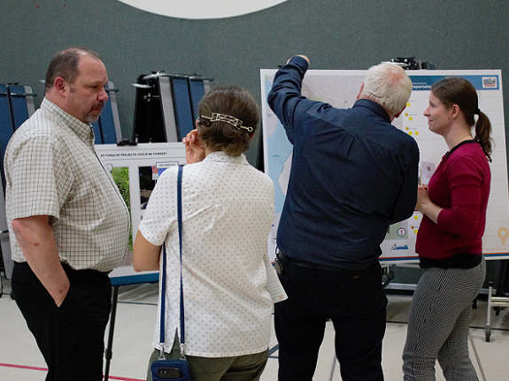 One person writes on a poster board while talking with another person while two other people engage in a separate discussion at a public workshop regarding the Transportation Master Plan.