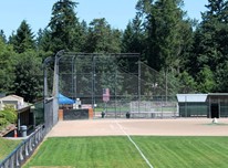 Baseball diamond at East Sammamish Park with two dugouts. Coniferous and deciduous trees loom in the background.
