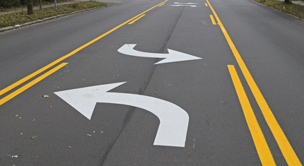 street with yellow lines and white arrows painted on it for traffic-control purposes