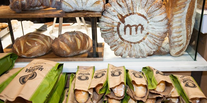 bread counter with Macrina Bakery loafs and a large round decorated with the Metropolitan Market logo in flour