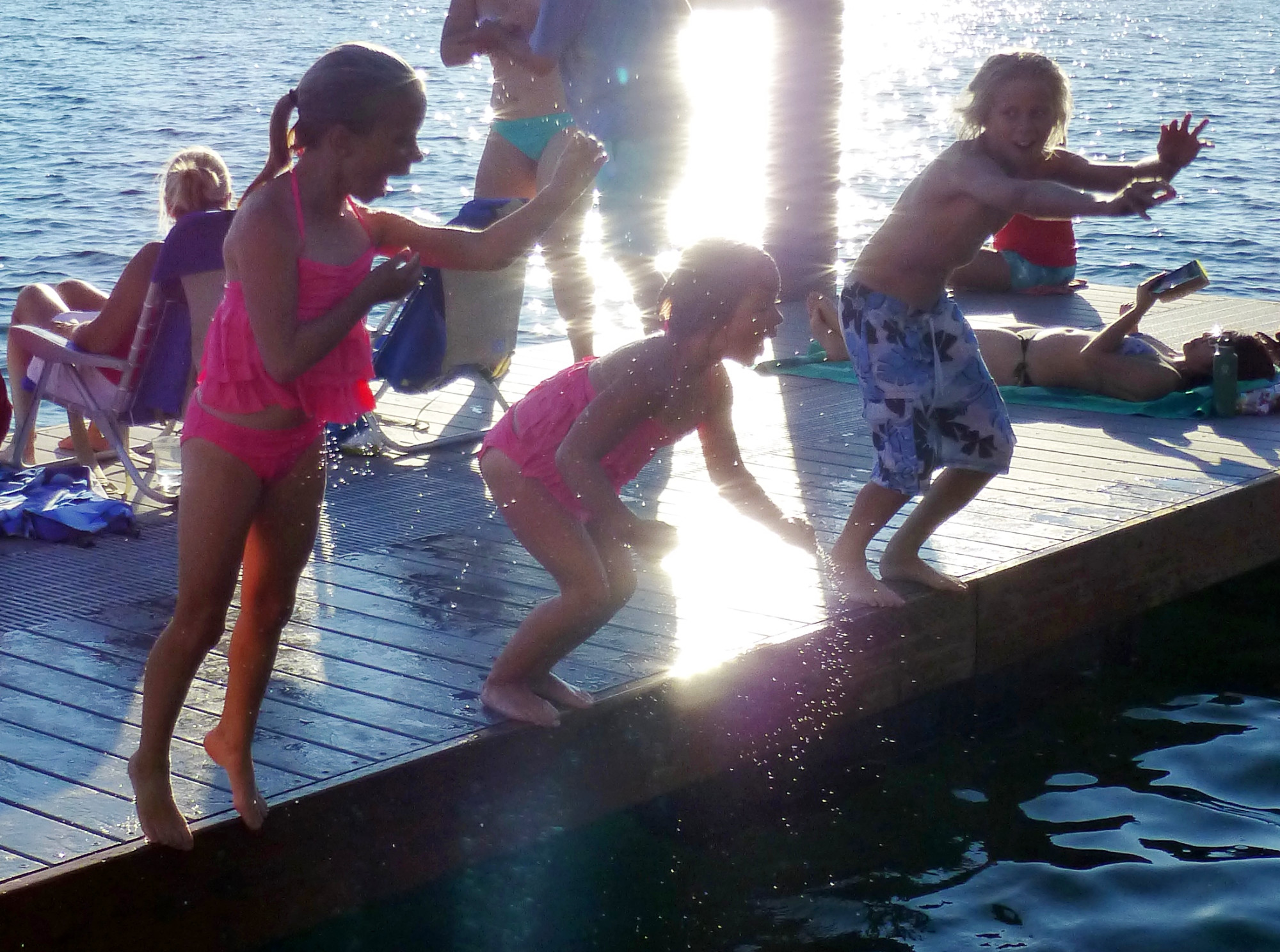 Three children jump off the dock, yelling with excitement, at Sammamish Landing Park on Lake Sammamish