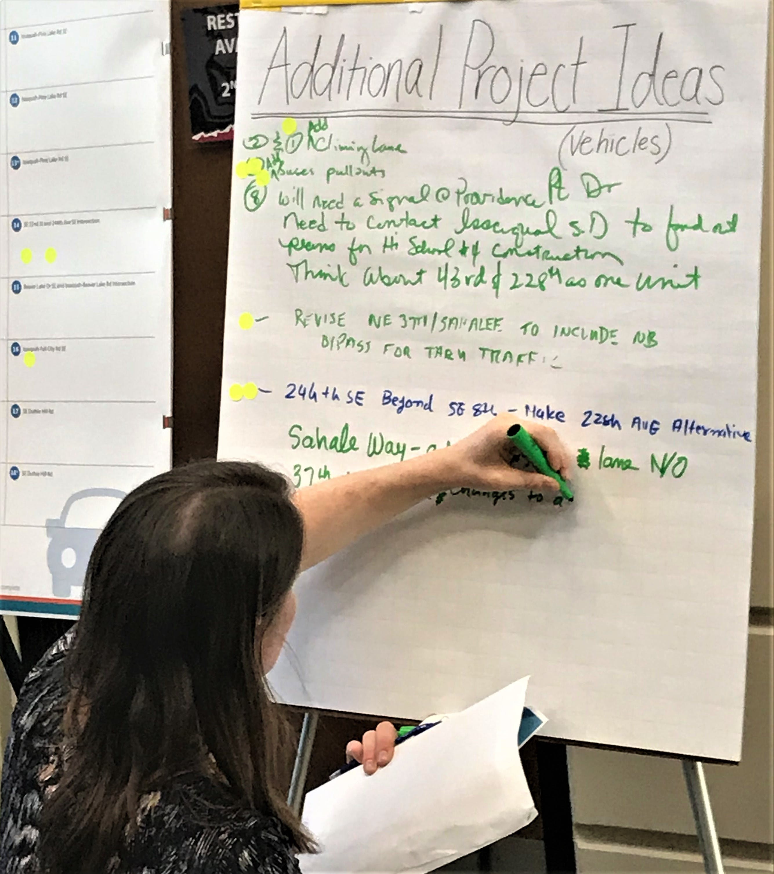 A woman adds additional ideas with a green marker onto a board during a public Transportation Master Plan workshop.