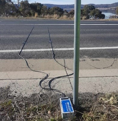 A traffic counter device sits on the side of the road with its cables reaching out into the street.