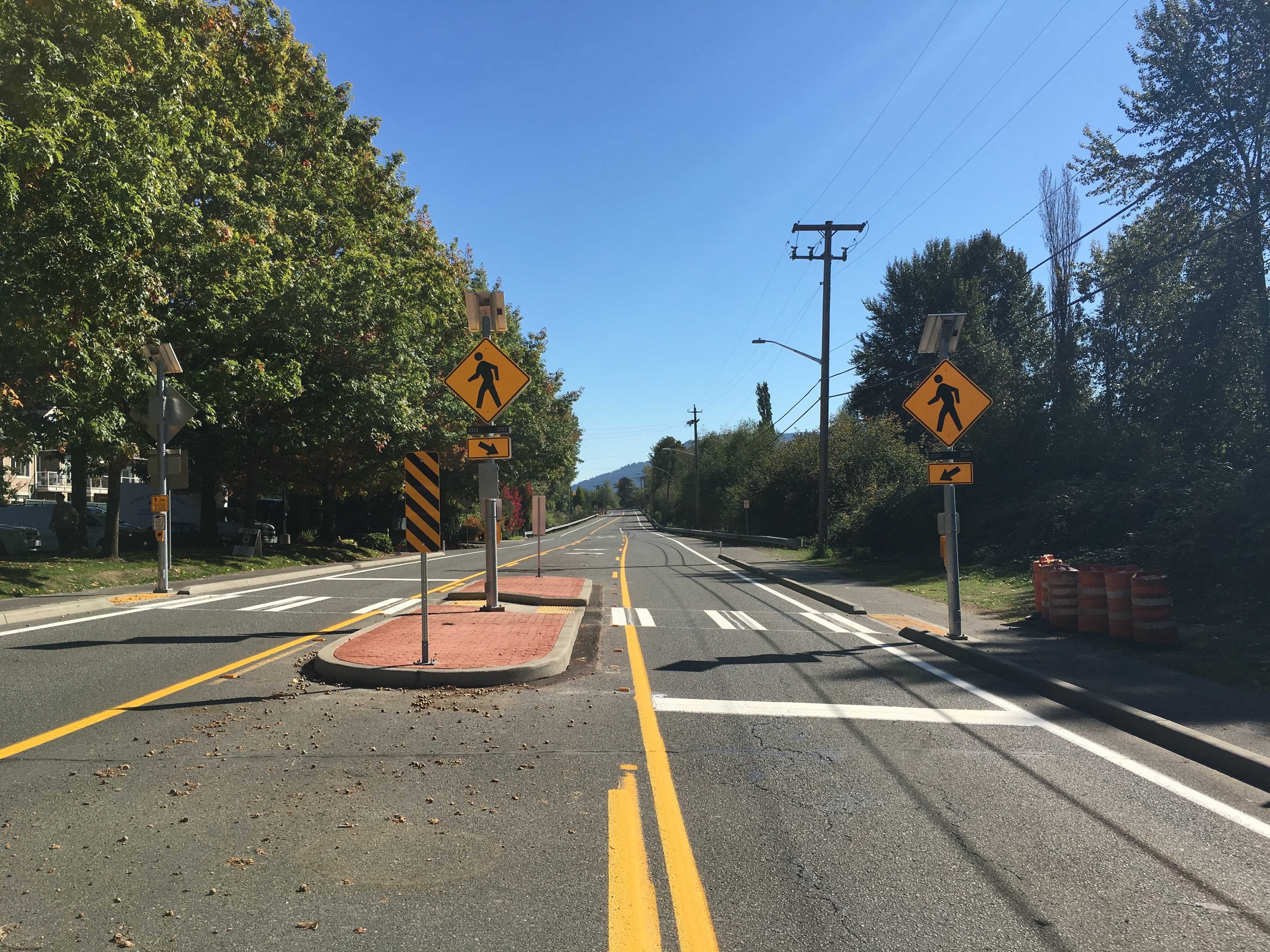 New crosswalk on East Lake Sammamish Parkway with crosswalk signage for vehicles. The street is lined with deciduous trees.