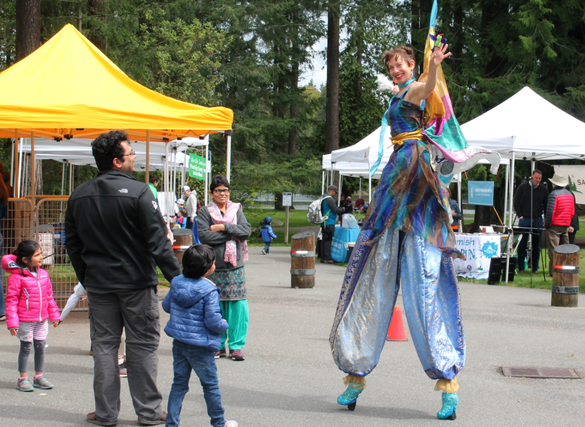 costumed stilt walker waves at Earth Day event while kids watch her