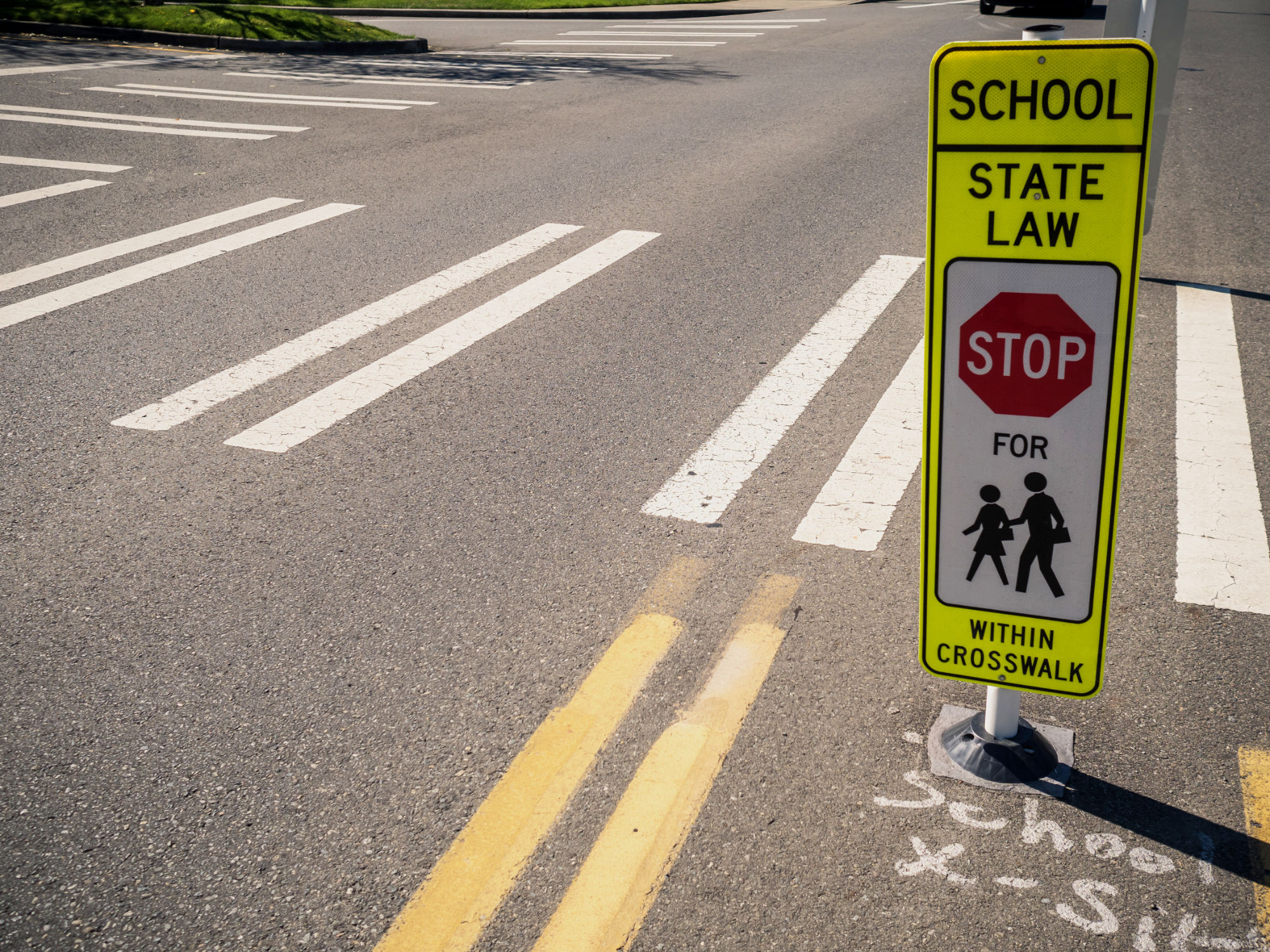 Close up of crosswalk in the street with sign next to it that reads "School - State Law - Stop for Pedestrians with the Crosswalk."
