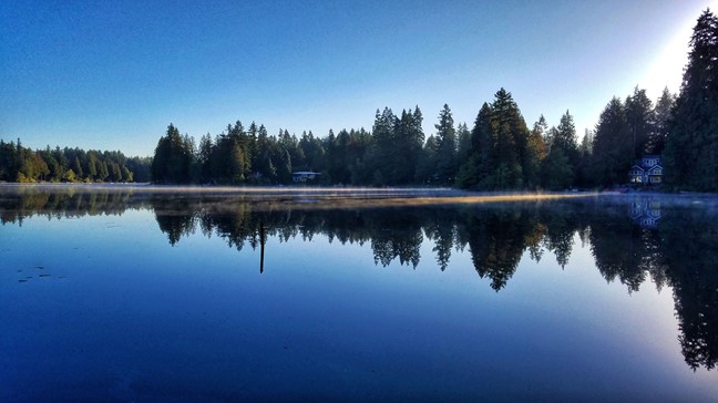 photo of beaver lake - blue water and blue sky with the evergreen trees on the shore reflecting clearly on the surface of Beaver Lake
