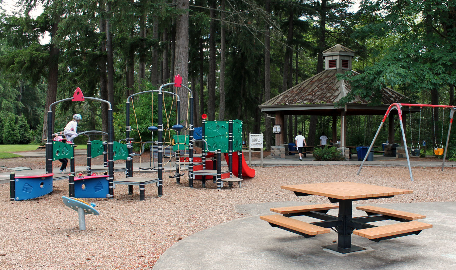 ebright creek park playground, with swingset and play structure over wood chip surface, in front of covered picnic shelter
