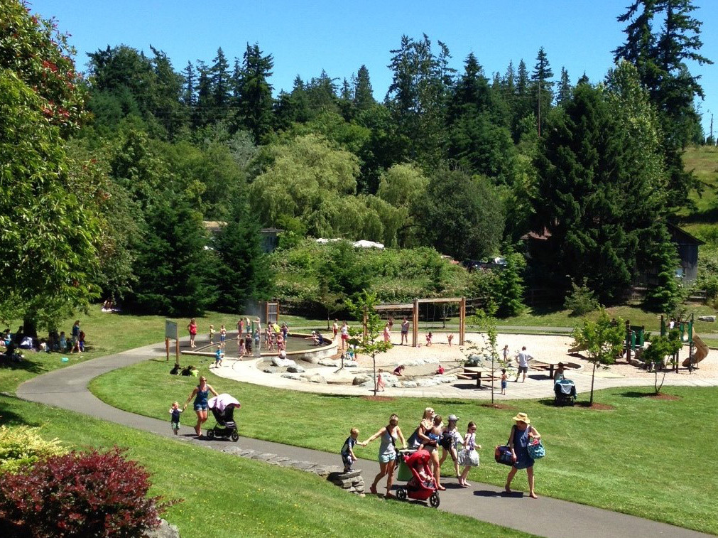 People walking along paved path in Sammamish Commons with the playground and spray park in the background.