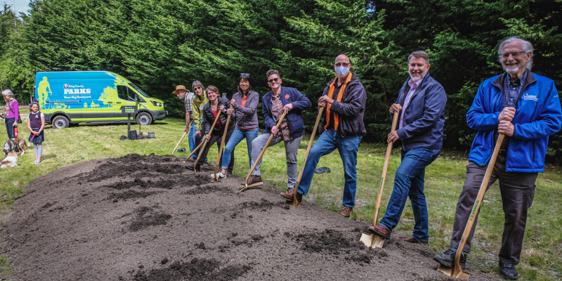 Several volunteers holding shovels next to pile of dirt with King County Parks van in the background.
