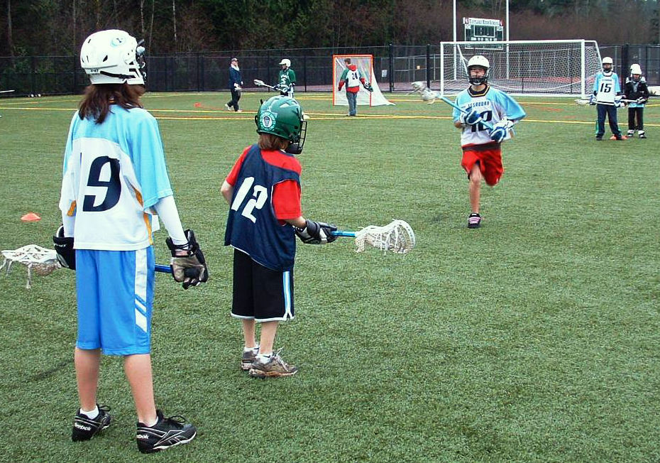 One player runs toward two others during a youth lacrosse drill at Eastlake Community Fields.