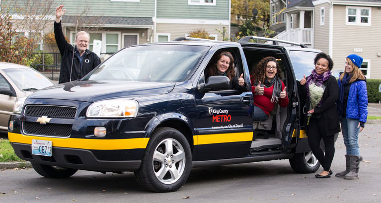 five people standing with a community van vehicle, flashing thumbs up and smiling