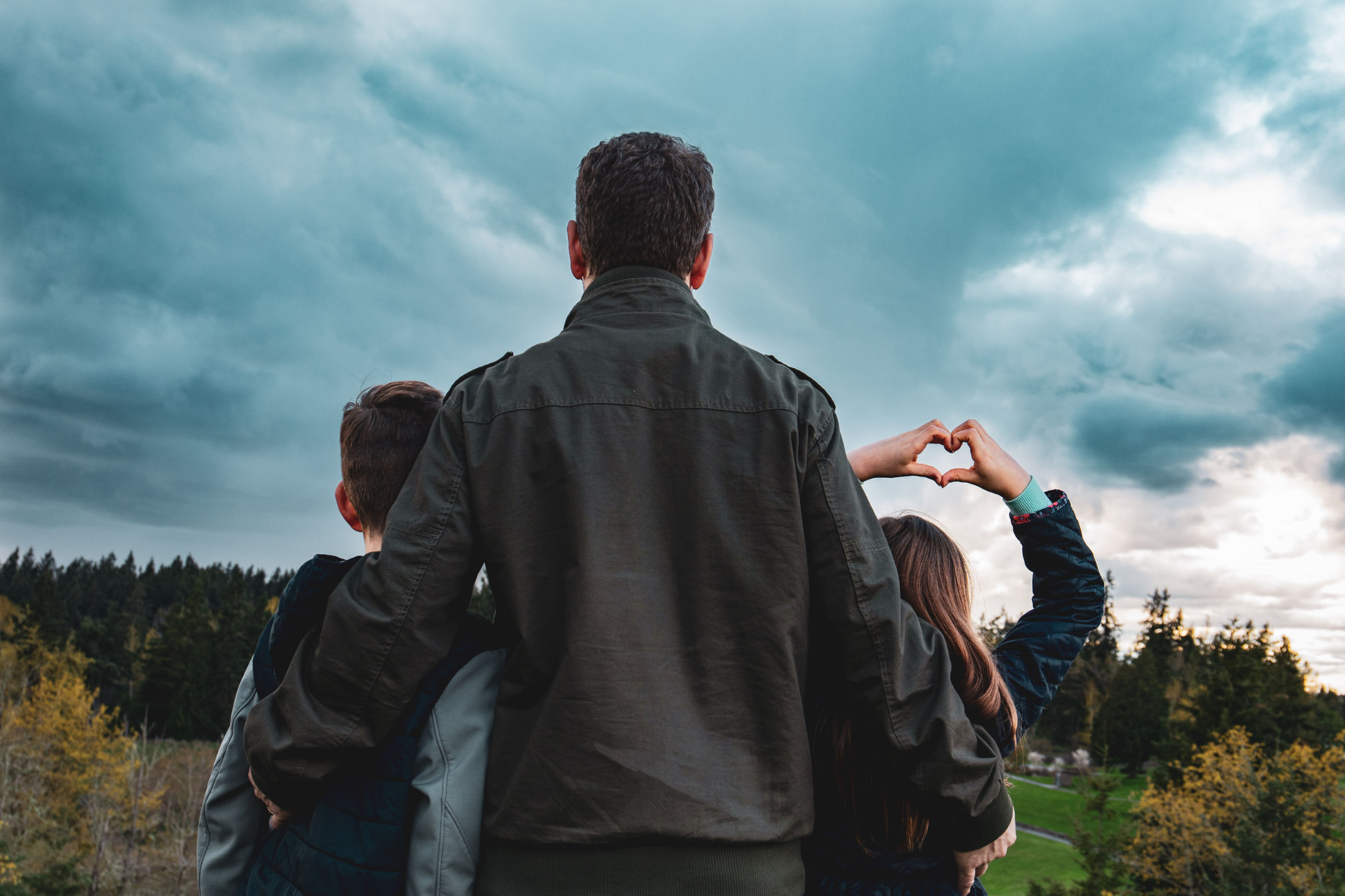 a family with adult and two kids stands looking out at a cloudy day on the commons, one child holding their hands up in a heart shape