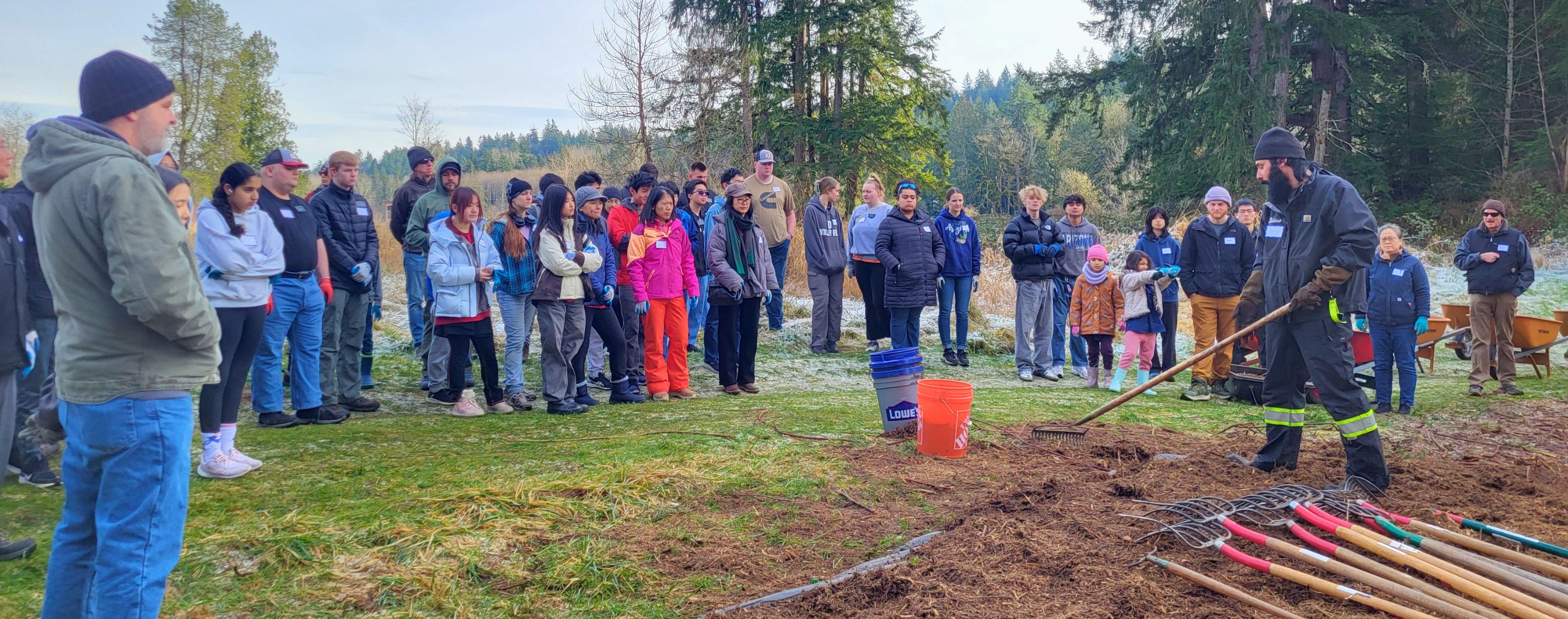 Restoration Specialist Sebastian Ritacco demonstrates trail restoration techniques with a pitch fork in front of gathered volunteers.