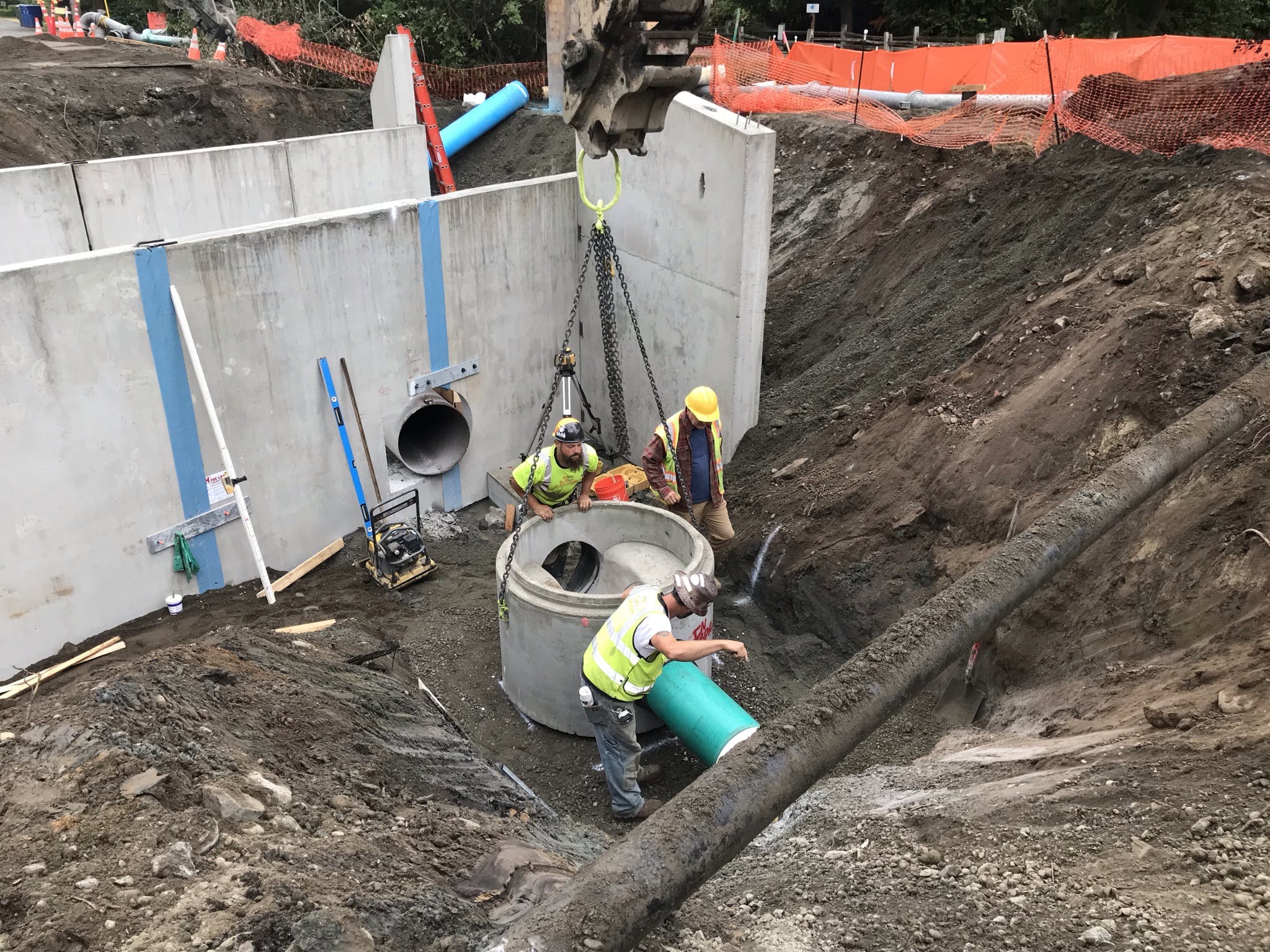 Three crew members coordinate the installation of a sewer manhole on the north side of the culvert at Ebright Creek.